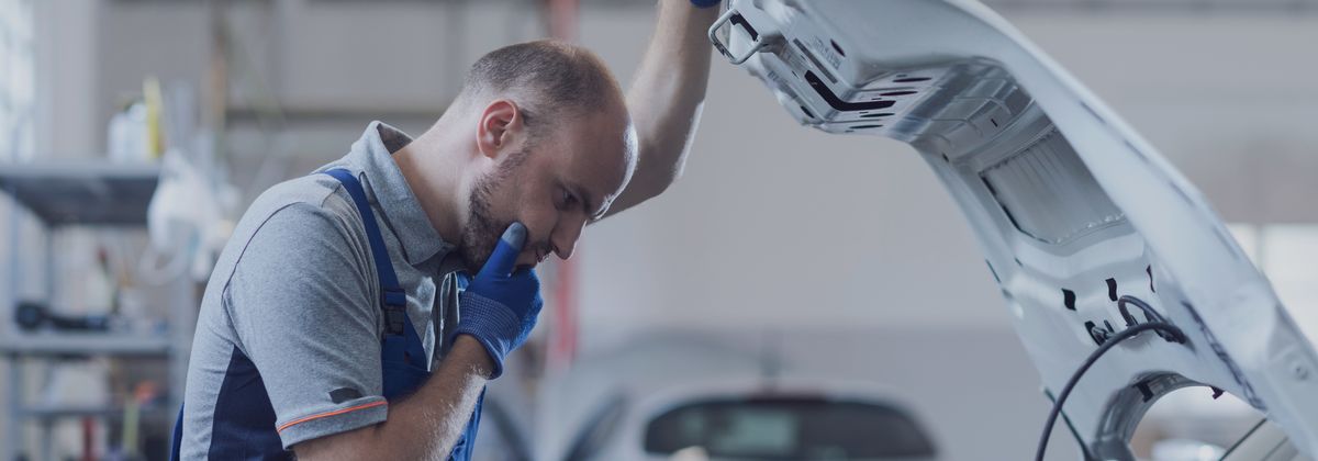 Tehnician de atelier care examinează compartimentul motorului, încercând să identifice cauza unei defecțiuni